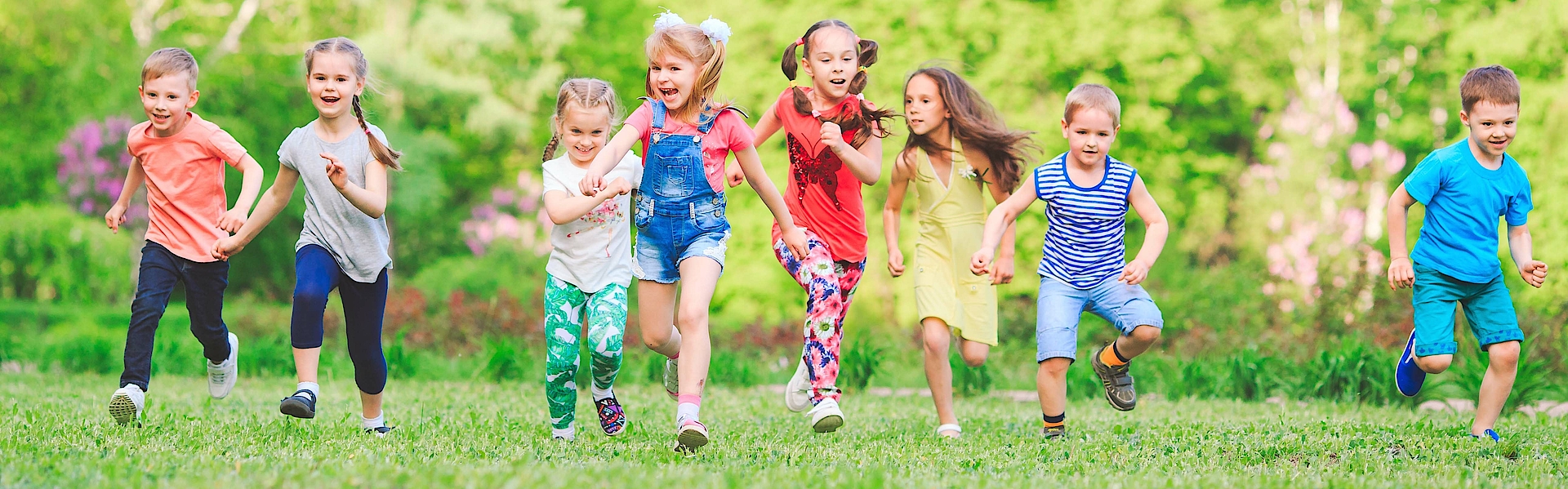 Eine Gruppe kleiner Kinder rennt über eine grüne Wiese. Sie haben Spaß zusammen und lachen ausgelassen. 