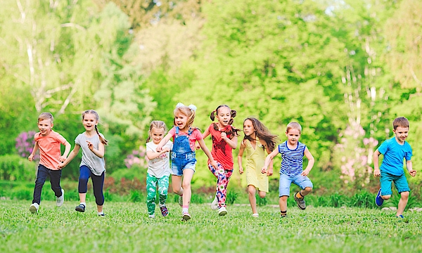 Eine Gruppe kleiner Kinder rennt über eine grüne Wiese. Sie haben Spaß zusammen und lachen ausgelassen. 