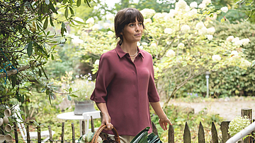 Frau mit einem Korb voller Gemüse steht im Garten.