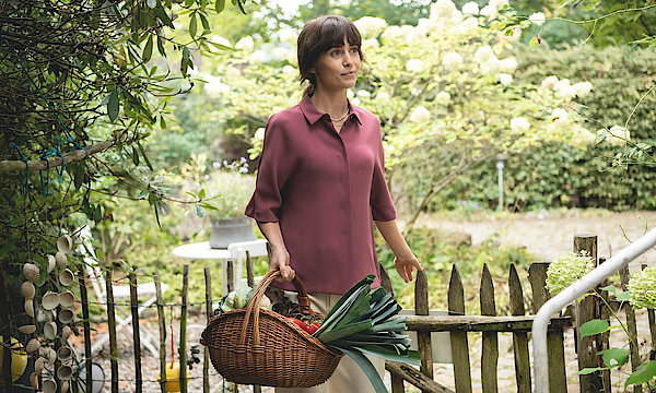 Frau mit einem Korb voller Gemüse steht im Garten.