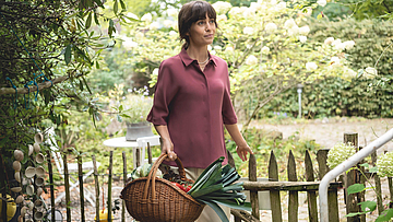 Frau mit einem Korb voller Gemüse steht im Garten.