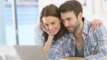 Frau stützt sich auf den Mann ab und beide schauen in den Laptop.