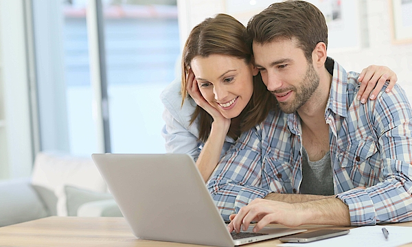 Frau stützt sich auf den Mann ab und beide schauen in den Laptop.