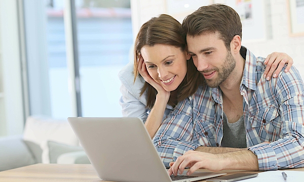 Frau stützt sich auf den Mann ab und beide schauen in den Laptop.