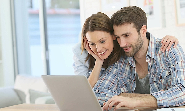 Frau stützt sich auf den Mann ab und beide schauen in den Laptop.