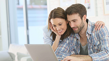 Frau stützt sich auf den Mann ab und beide schauen in den Laptop.