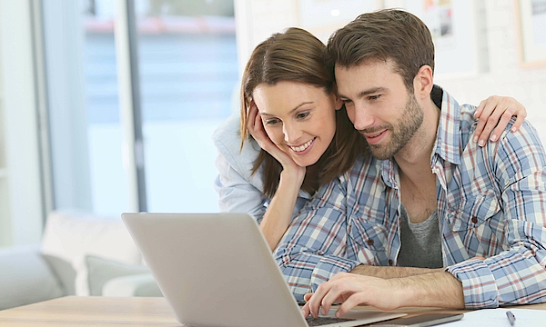 Frau stützt sich auf den Mann ab und beide schauen in den Laptop.