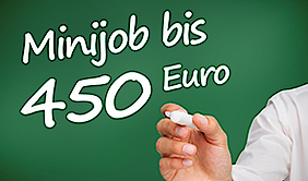 Handschrift mit einem weißen Stift auf einem grünen Untergrund: "Minijob bis 450 Euro". Der Stift wird von einer Hand gehalten.