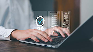 Hände auf Laptop es werden Symbole: Compliance, Qualitätssicherung und mehr dargestellt.