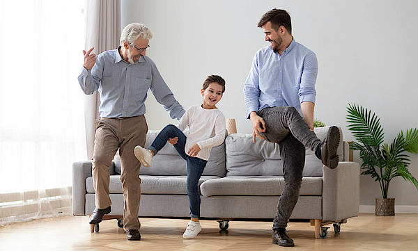 Opa, Kind und Vater machen gemeinsam Gymnastik vor einem grauen Sofa.