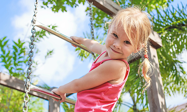 Mädchen ist auf einem Spielplatz und klettert an einem Klettergerüst.