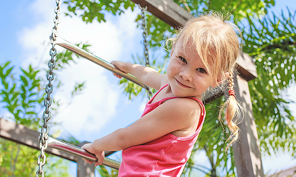 Mädchen ist auf einem Spielplatz und klettert an einem Klettergerüst.