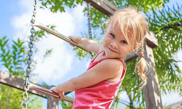 Mädchen ist auf einem Spielplatz und klettert an einem Klettergerüst.