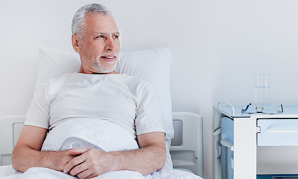 Ein männlicher Patient liegt im Krankenbett. Er blickt aus dem Fenster.