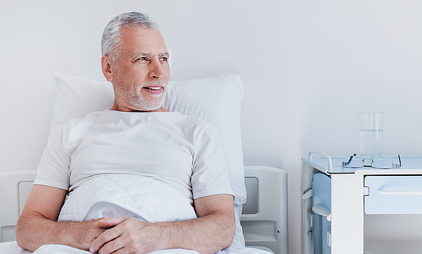 Ein männlicher Patient liegt im Krankenbett. Er blickt aus dem Fenster.