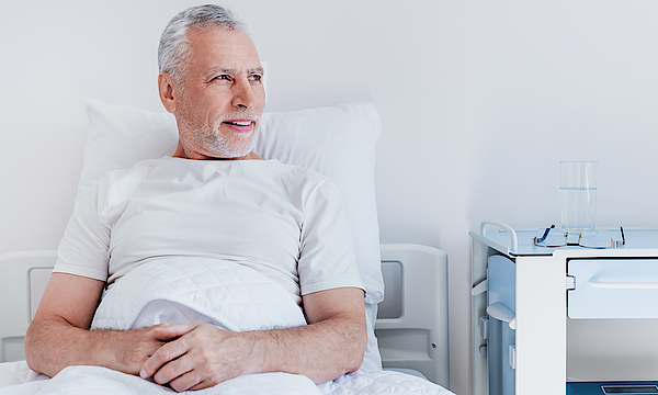 Ein männlicher Patient liegt im Krankenbett. Er blickt aus dem Fenster.