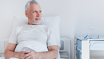 Ein Mann hat mit der Krankenhaussuche die für ihn passende Klinik gefunden. Er befindet sich bereits im Krankenbett und schaut in die Ferne
