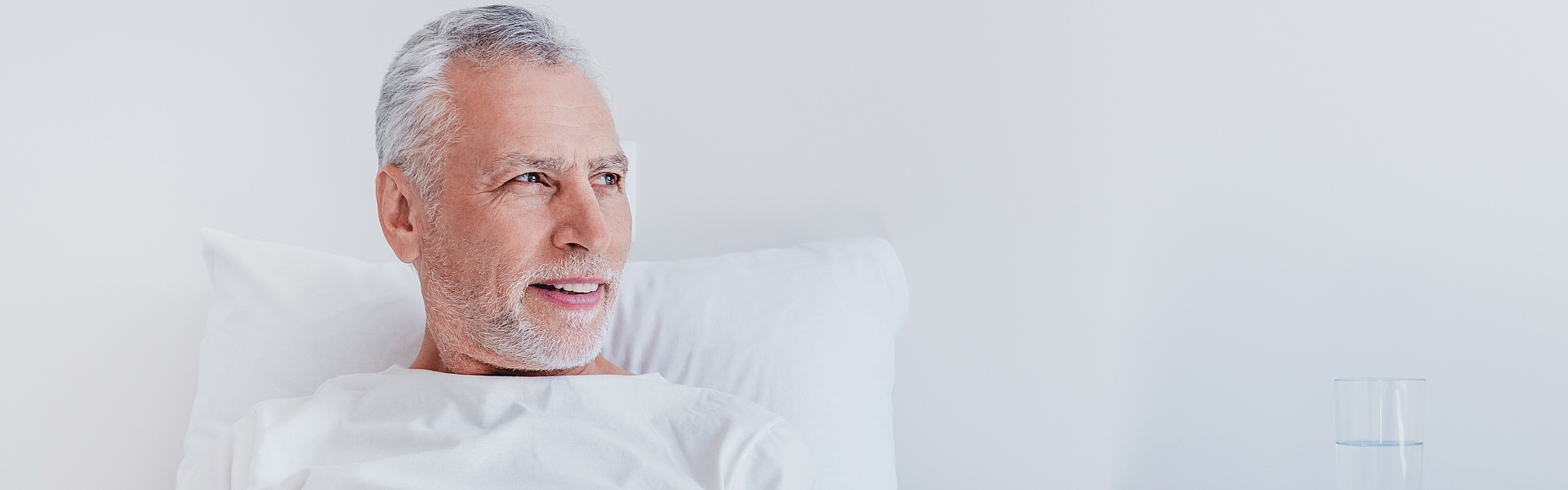 Ein Mann hat mit der Krankenhaussuche die für ihn passende Klinik gefunden. Er befindet sich bereits im Krankenbett und schaut in die Ferne.