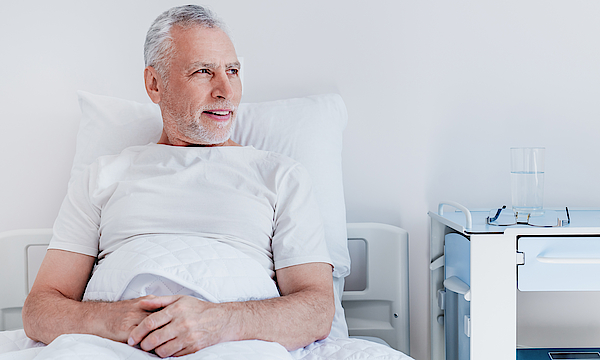 Ein männlicher Patient liegt im Krankenbett. Er blickt aus dem Fenster.