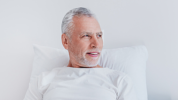 Ein männlicher Patient liegt im Krankenbett. Er blickt aus dem Fenster.