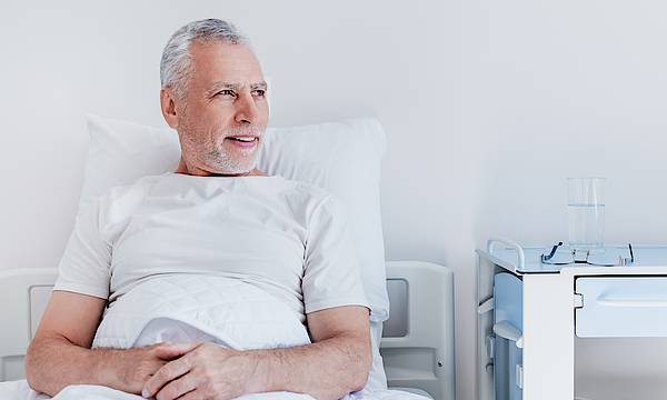 Ein männlicher Patient liegt im Krankenbett. Er blickt aus dem Fenster.