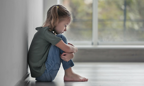 Ängstliches und trauriges kleines Mädchen sitzt im Haus auf dem Boden vor einem Fenster.