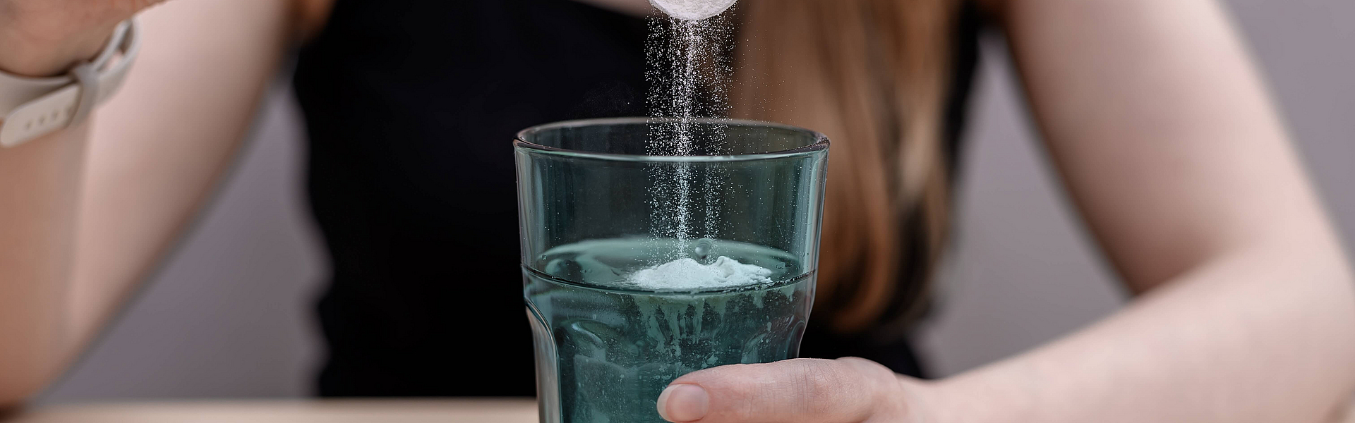 Frau löst Kreatin in einem Glas Wasser auf. 