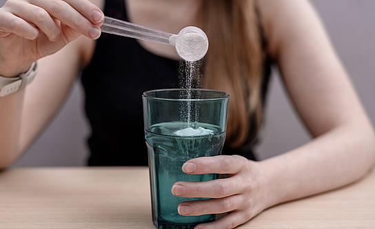 Frau löst Kreatin in einem Glas Wasser auf. 