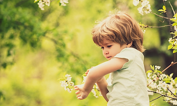 Kind ist draußen auf einer Wiese mit Blüten und kratzt sich am Arm.