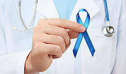 Nahaufnahme eines Arztes, der eine blaue kleine Schleife für Darmkrebs hochhält.
