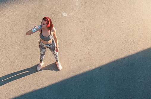 Frau in Sportkleidung steht in der Sonne und trinkt nach dem Sport
