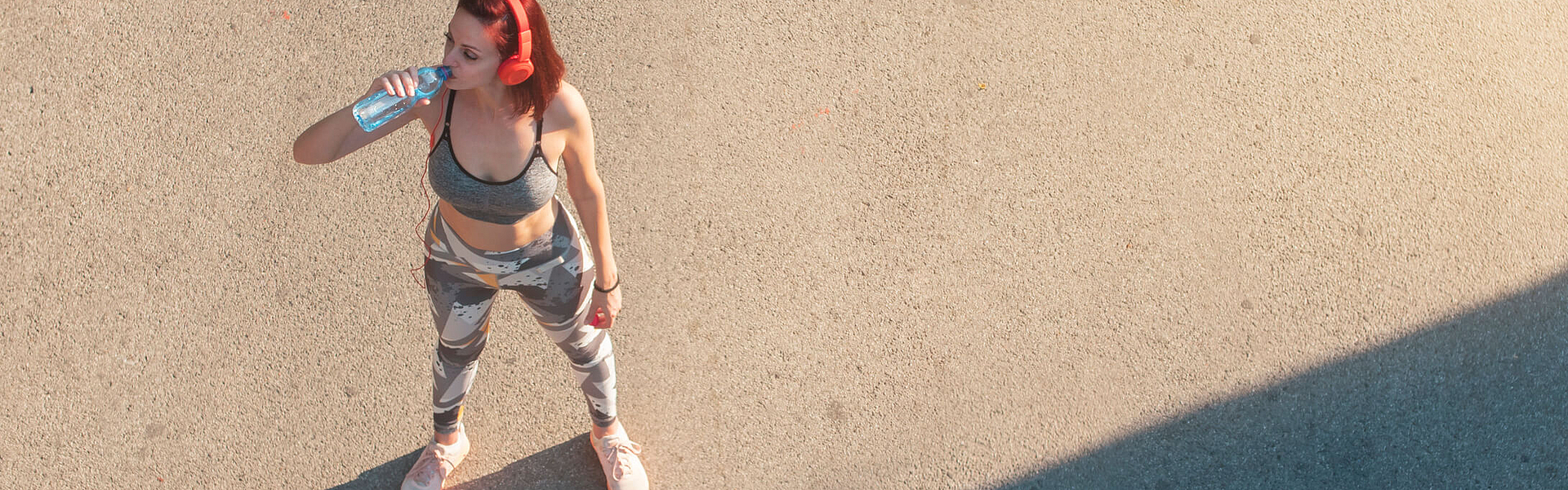Frau in Sportkleidung steht in der Sonne und trinkt nach dem Sport 