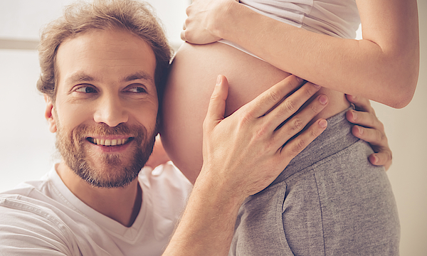 Ein Mann drückt seinen Kopf an den schwangeren Bauch.