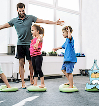 Ein Mann macht Sport mit kleinen Kindern und PFIFFIX auf Yoga-Steinen.