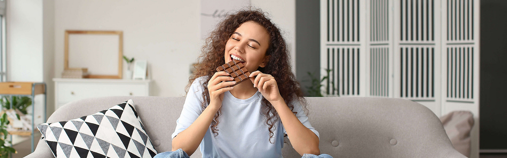 Junge Frau sitzt auf dem Sofa und Schokolade isst.