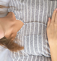 Eine schwangere Frau liegt auf dem Bett, sie umfasst mit beiden Händen ihren Bauch.