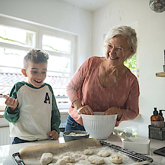 Enkel steht mit der Oma in der Küche, sie backen gemeinsam. Das Backblech ist schon fast voll.