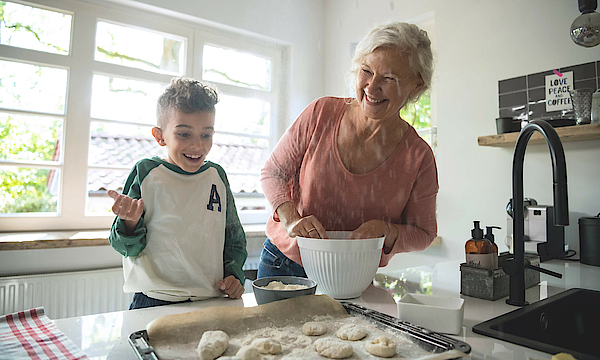 Enkel steht mit der Oma in der Küche, sie backen gemeinsam. Das Backblech ist schon fast voll.