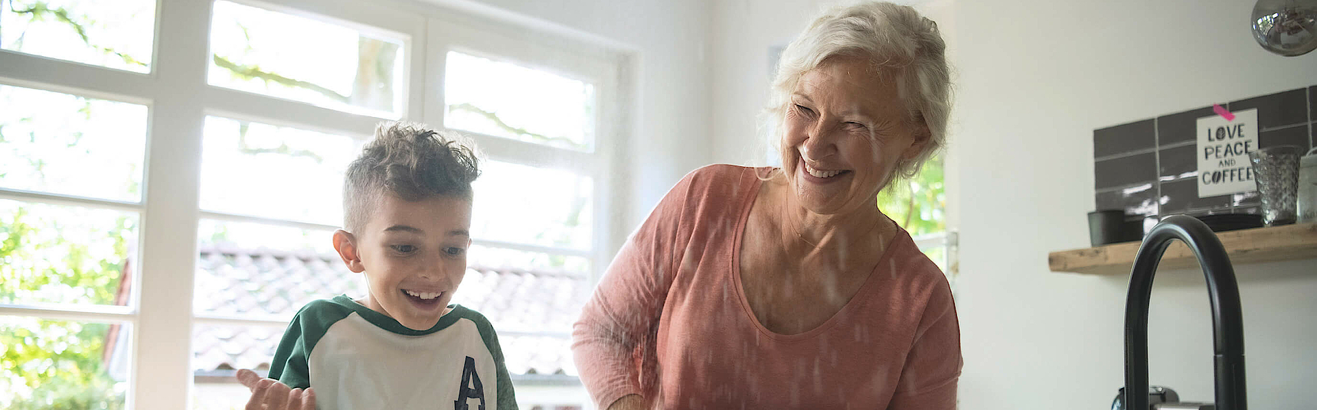 Enkel steht mit der Oma in der Küche, sie backen gemeinsam. Das Backblech ist schon fast voll.