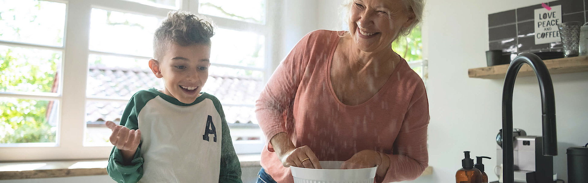 Enkel steht mit der Oma in der Küche, sie backen gemeinsam. Das Backblech ist schon fast voll.