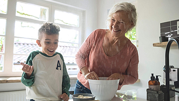 Enkel steht mit der Oma in der Küche, sie backen gemeinsam.