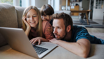 Fröhliche Familie auf dem Sofa mit Laptop.