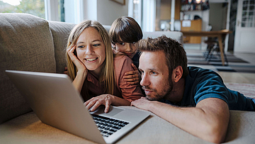 Fröhliche Familie auf dem Sofa mit Laptop.