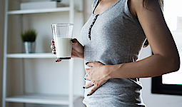 Eine Frau hält ein Glas mit Milch in der rechten Hand. Mit der anderen Hand hält sie sich den Bauch.