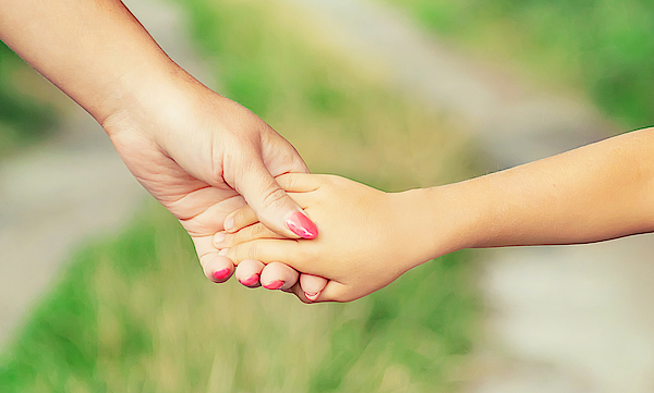 Eine Erwachsene hält die Hand eines Kindes. Sie laufen auf einem Weg. Es sind nur die Hände der Personen zusehen. 