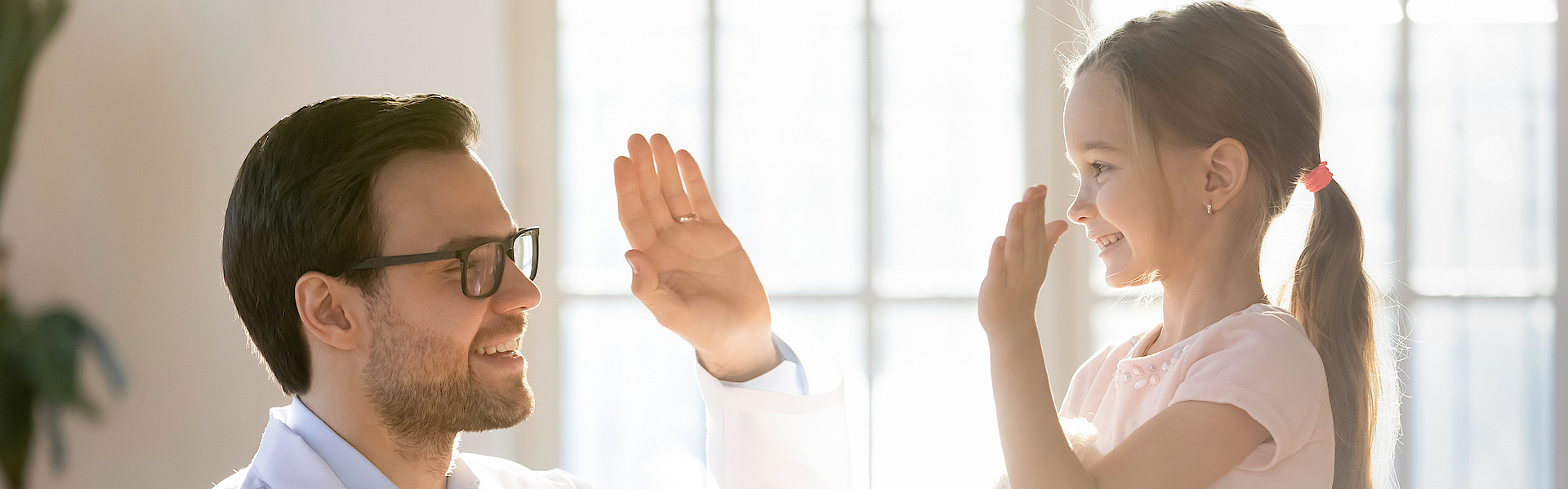 Ein kleines Mädchen ist beim Kinderarzt. Es sitzt auf dem Untersuchungstisch. Es ist fröhlich. Der Arzt ihr gegenüber auch. Sie geben sich High-Five.