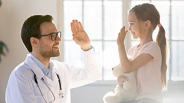 Ein kleines Mädchen ist beim Kinderarzt, sie sitzt auf dem Untersuchungstisch. 