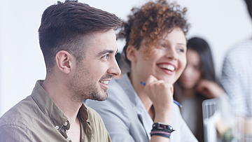Zwei junge Menschen schauen zusammen auf einen Laptop. Sie freuen sich.