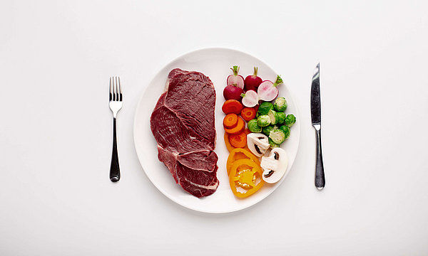 Auf einem Teller liegt Gemüse, daneben ein Stück Fleisch. Neben dem Teller liegen Messer und Gabel.