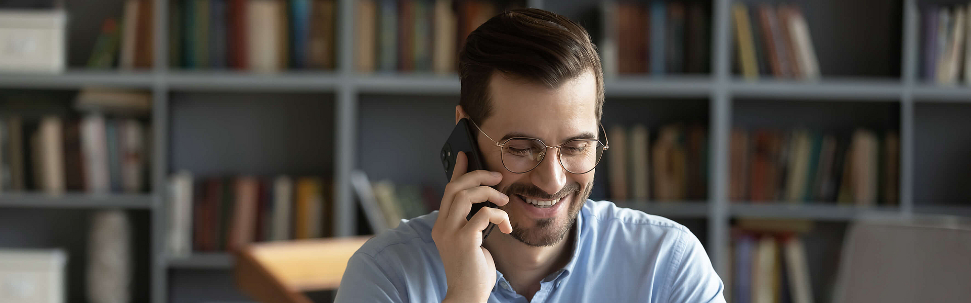 Geschäftsmann mit einer Brille telefoniert und sitzt am Schreibtisch mit seinem Laptop.